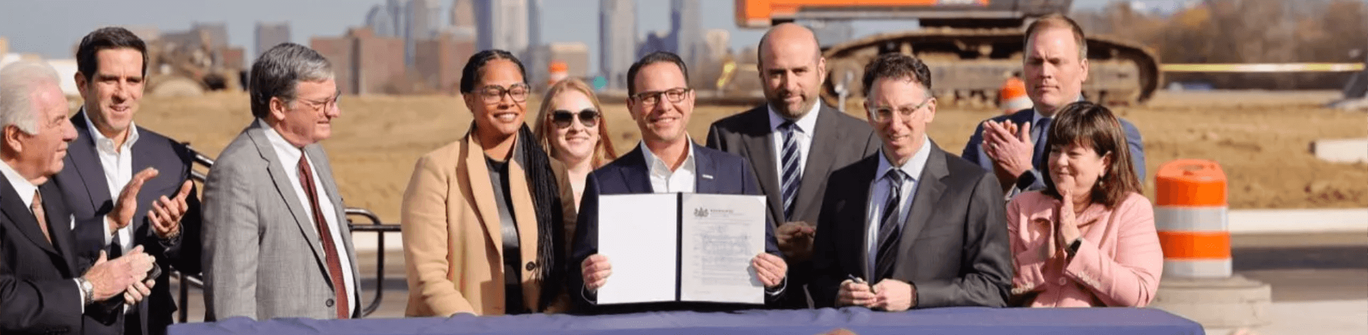 Governor Josh Shapiro, surrounded by a group of government officials and business leaders, smiles and shows an exectutive order document for the just-announced Permit Fast Track program.